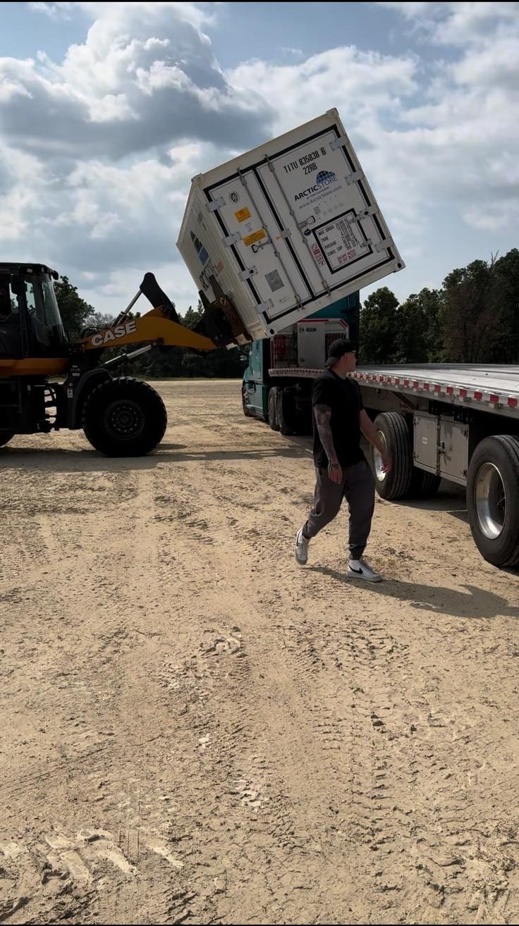 Wheel loader placing a refrigerated container on a flatbed trailer at a field site